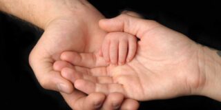 Two Caucasian adult hands, one in the other, with a baby's hand in them.