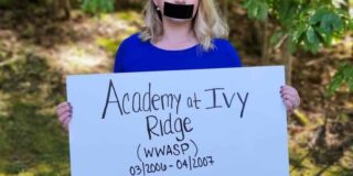 a thin young woman with blond hair holds a sign in front of her with problems she's faced due to attendance at Academy of Ivy Ridge. Her mouth is covered with black tape.