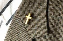 A suit coat lapel is shown with a gold cross pin on it.
