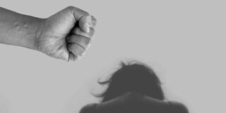 In this B&W image a fist is shown close to camera, a bowed head with longer hair is further away, implying violence.