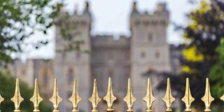 Image shows gold finials on black wrought iron fence with a castle like building with two towers blurred in the distance.