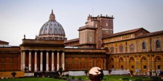 A view of the Vatican dome and surrounding buildings is seen from a distance.