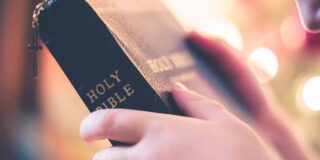 A person holds a bible in both hands with their head bowed toward it.