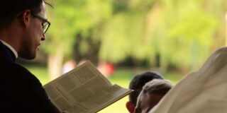 A priest is seen outdoors and from the side reading an open Bible.
