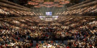 The stadium-like interior of a mega church is shown filled with people.