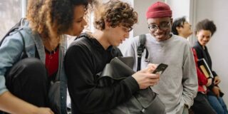 A diverse group of college students are shown looking at the phone of one.
