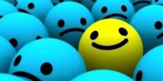 Yellow smiley happy face ball among blue sad face balls.