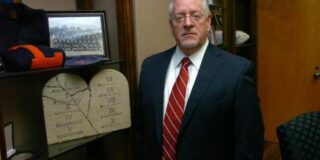 Dr. Joe Aguillard in his office standing next to a 10 commantments plaque