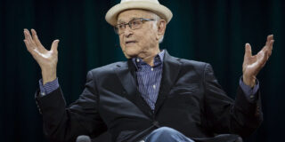 Norman Lear sits and speaks with his palms raised to his sides.