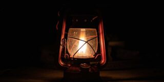 A single lit gas lantern sits by itself in the dark.
