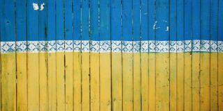 The colors of the Ukraine flag are painted across wooden fence boards.