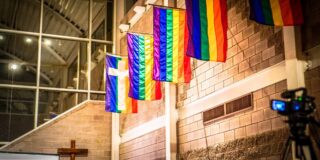 Pride flags hang on an interior stone wall.